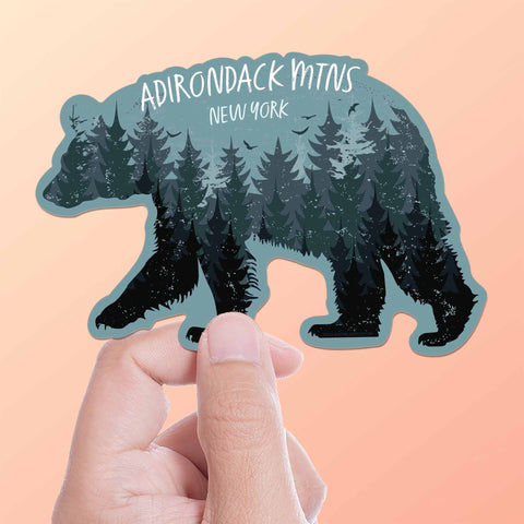 Cute Black Bear Adirondacks New York Sticker in Womans Hand on Blue Background