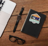 Adirondack Park Mountain Sticker on Journal with Laptop and Watch on Wood Desk in Office