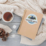 Adventure Awaits Snowmobile Sticker on notebook next to cozy hot tea table