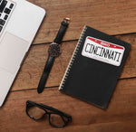 Cincinnati Sticker on Journal with Laptop and Watch on Wood Desk in Office