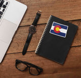 Cute Colorado Sticker on Journal with Watch and Laptop on Wood Desk in Office