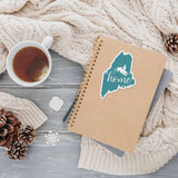 Cute Maine Snowmobile Sticker on Journal with Mug of Tea and Winter Sweater