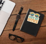 Out of Office Camping Sticker on Journal with Macbook and Watch on Wood Desk in Office