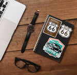 Set of All Route 66 Stickers on Journal with Laptop and Watch on Wood Desk in Office