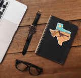 Southwest Texas Sticker on Journal with Laptop and Watch on Wood Desk in Office