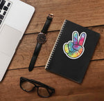Tie Dye Peace Sign Sticker on Journal with Laptop and Watch on Wood Desk
