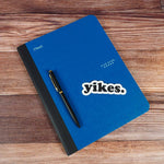 Yikes Funny Sticker on Notebook with Pen on Wood Desk
