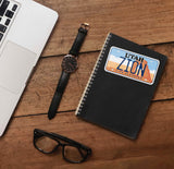 Zion National Park Sticker on Journal with Laptop and Watch on Wood Desk in Office